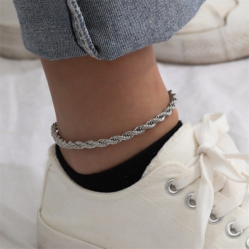 Bracelet de cheville en acier inoxydable argenté, maille torsadée fine porté avec baskets blanches.
