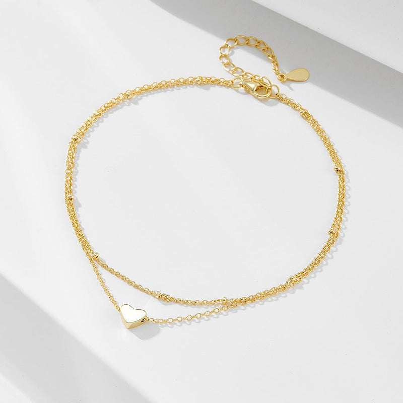 Bracelet de cheville en or avec motif cœur lisse et chaînette fine double rang pour femme.