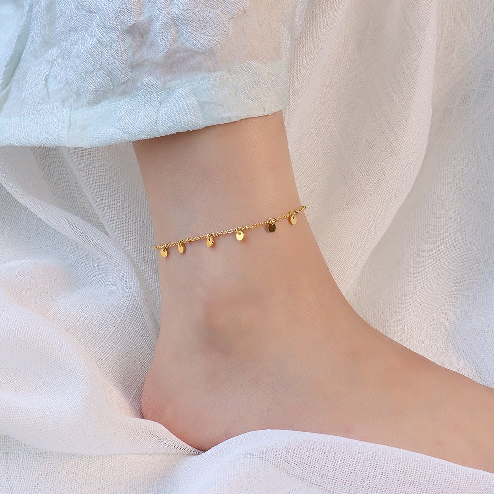 Bracelet de cheville en titane doré avec multiples petits médaillons ronds suspendus.