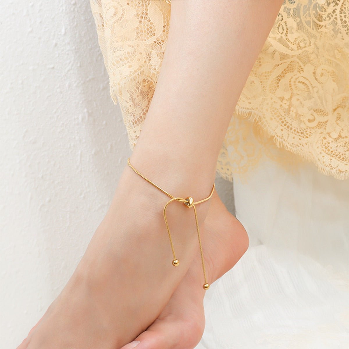 Bracelet de cheville coulissant en titane couleur or avec pendentifs ronds sur peau féminine.