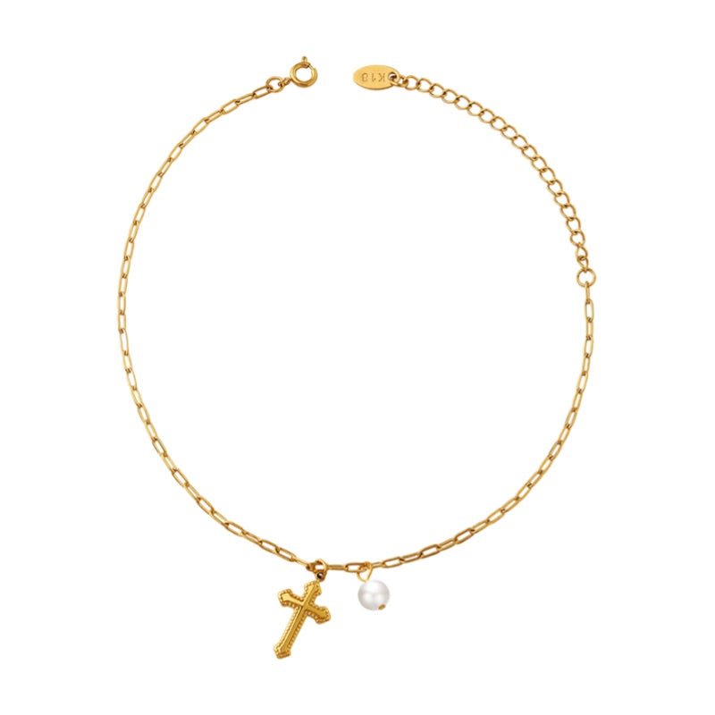 Bracelet de cheville or en titane avec chaîne fine, croix chrétienne et petite perle nacrée suspendue.