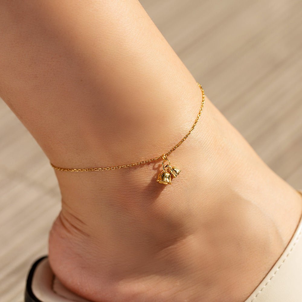 Bracelet de cheville en titane doré avec pendentif cloches délicates sur peau féminine.