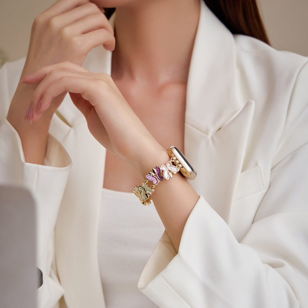 Bracelet Apple Watch or avec motifs papillons multicolores porté sur poignet féminin en veste blanche.