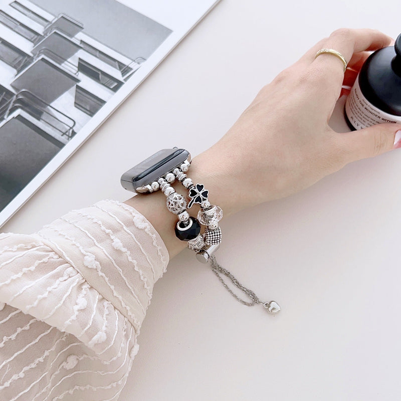 Bracelet double-rangs rose pour Apple Watch avec breloques argentées variées sur poignet féminin.