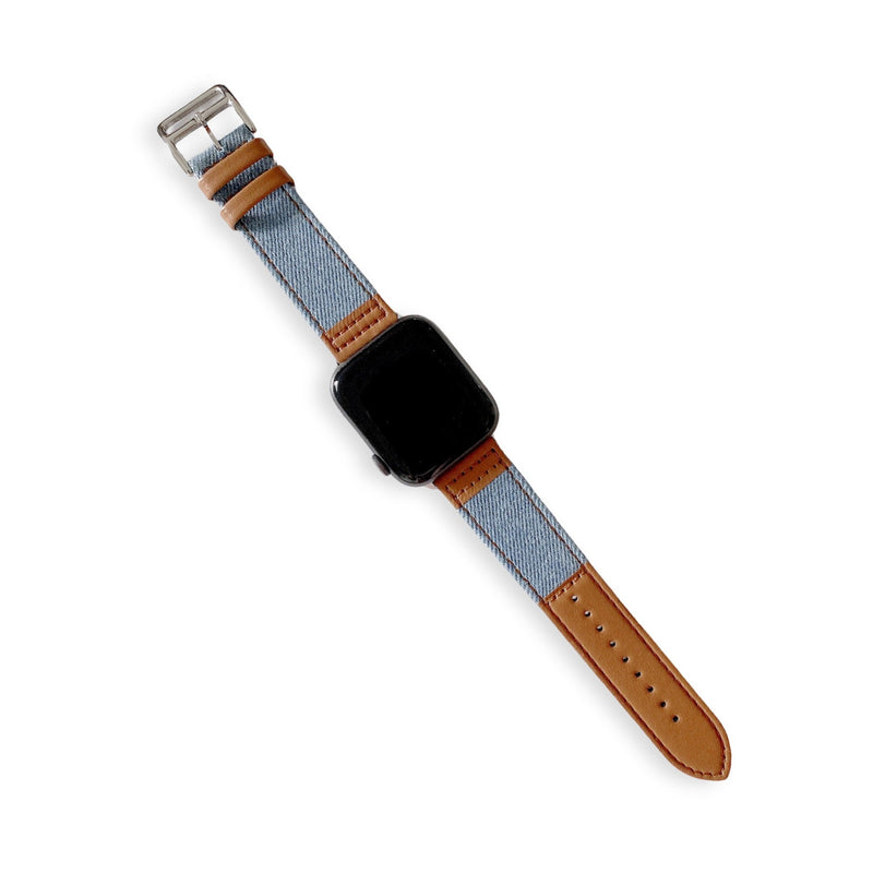 Bracelet Apple Watch en cuir marron et denim bleu clair, boucle argentée, couture orange visible.