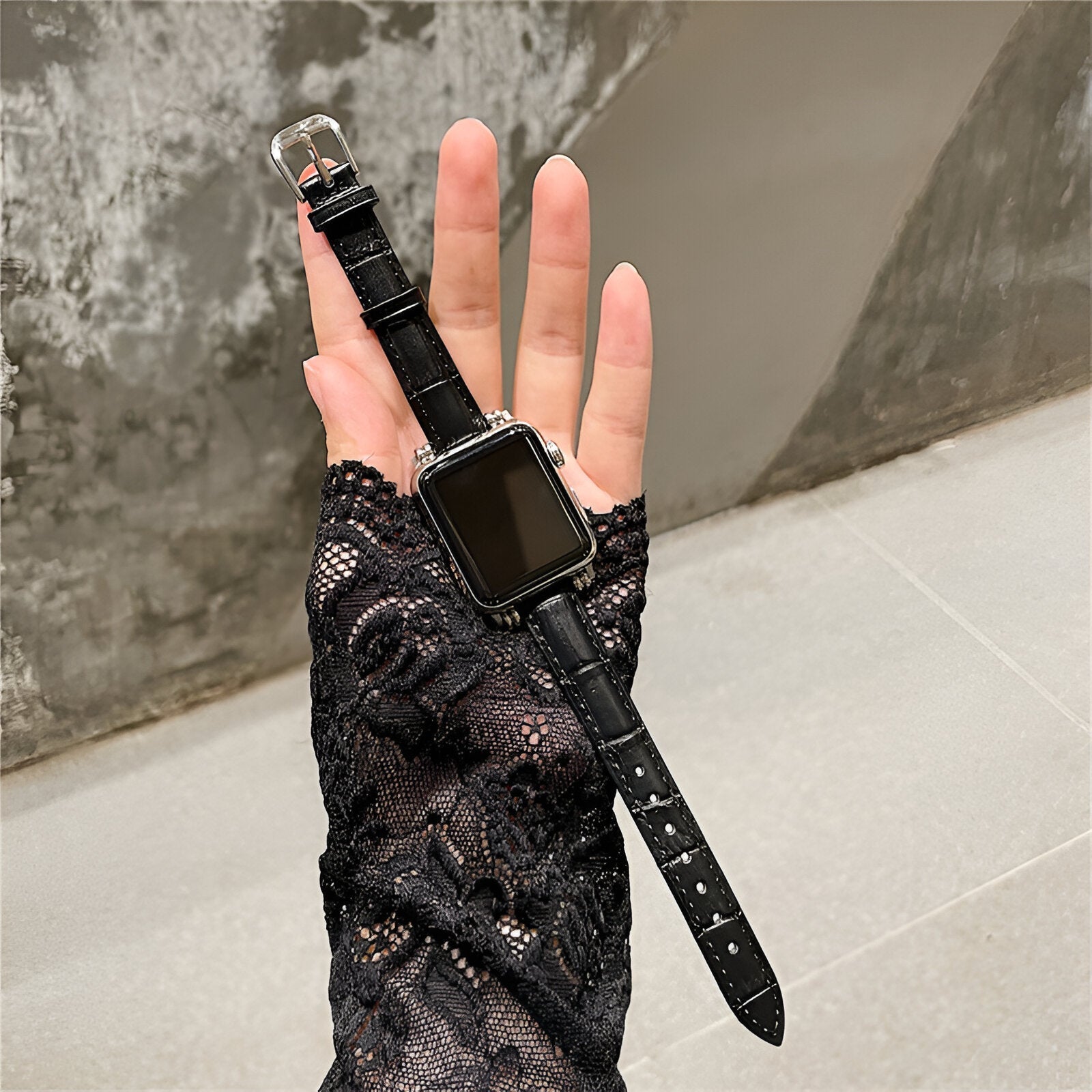 Bracelet Apple Watch noir en microfibre avec boucle argentée porté sur main gantée de dentelle noire.