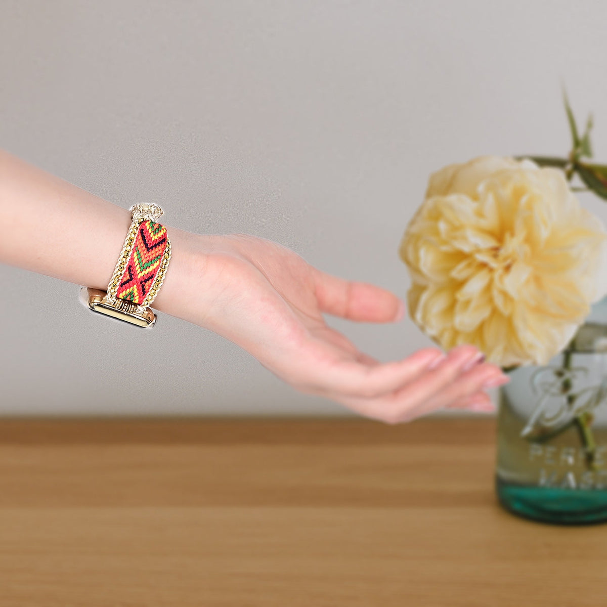 Bracelet Apple Watch en nylon rouge avec motif cristal élégant porté au poignet féminin avec fleur jaune floue en.