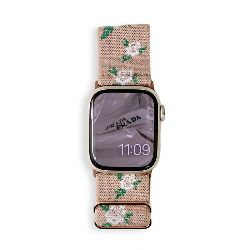Bracelet Apple Watch en nylon rose à motifs floraux blancs et verts, boucle métallique noire.