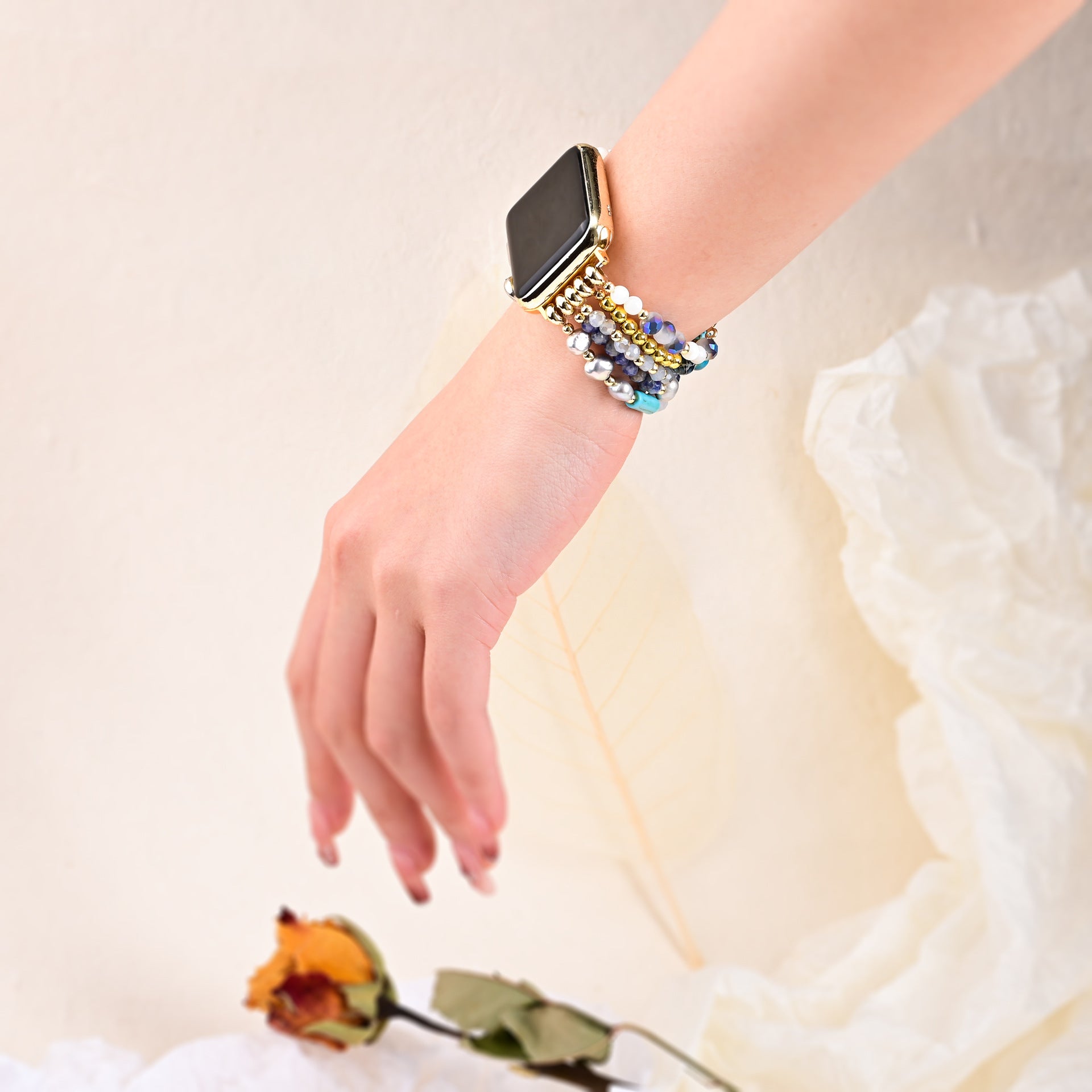 Bracelet Apple Watch multicolore en pierres de cristal brillantes porté sur poignet féminin avec robe blanche en tissu léger.