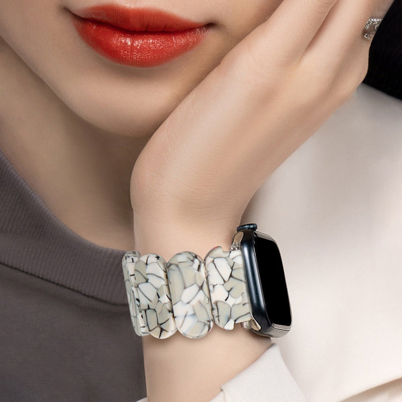Bracelet Apple Watch en résine blanc tacheté motifs noirs, style large et arrondi, porté au poignet féminin.