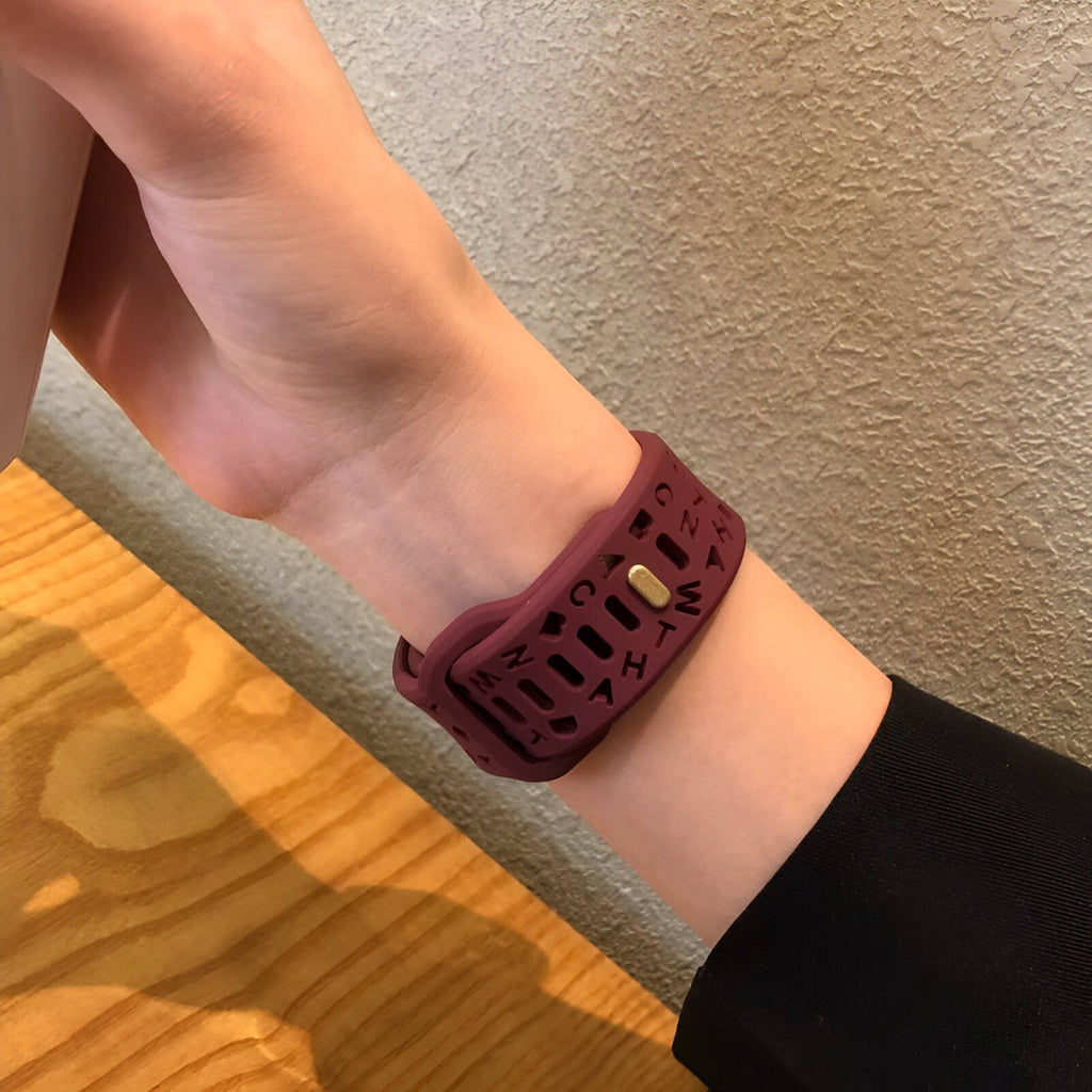 Bracelet en silicone bordeaux perforé pour Apple Watch porté au poignet féminin.