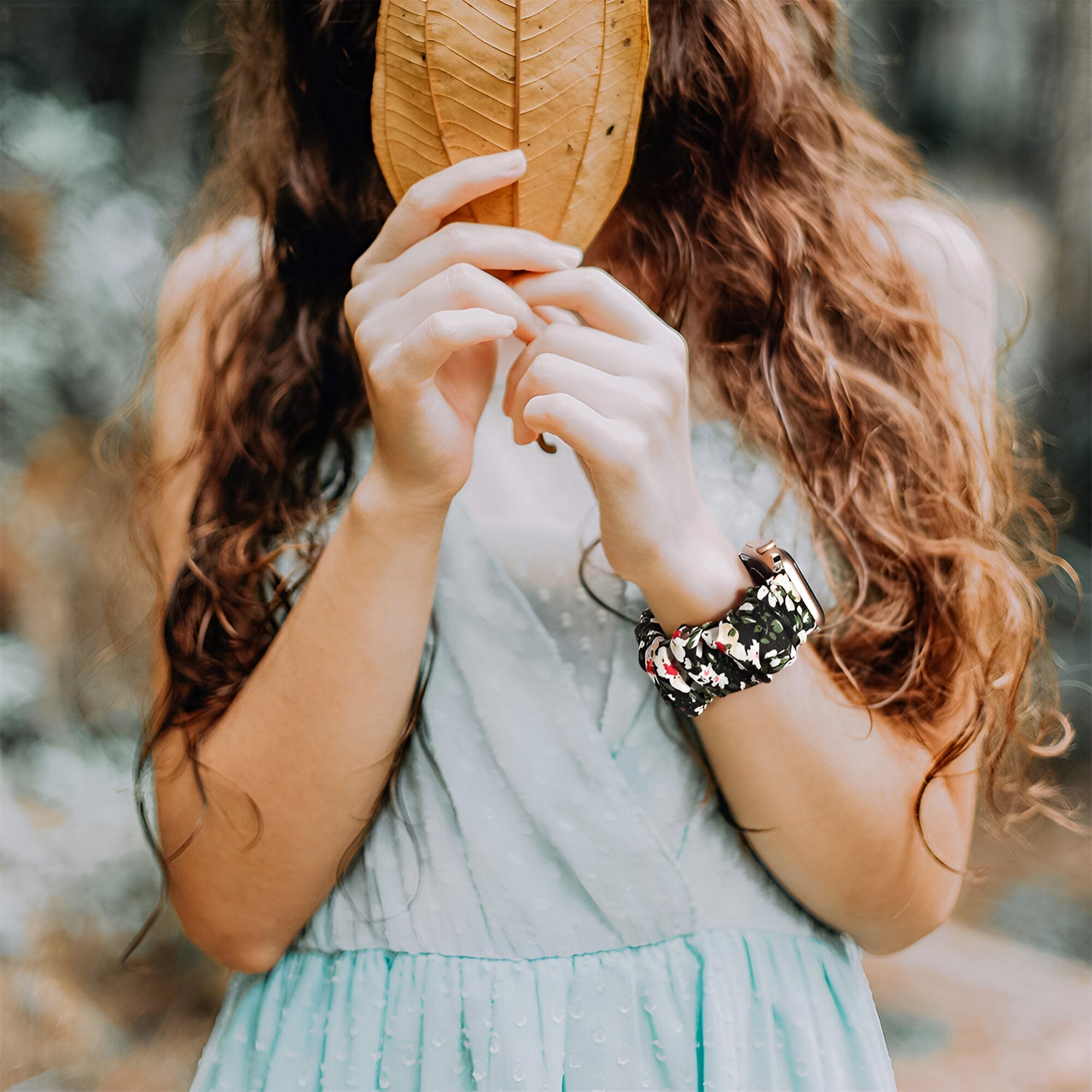 Bracelet Apple Watch élastique en tissu floral multicolore porté par femme avec robe bleue pâle.