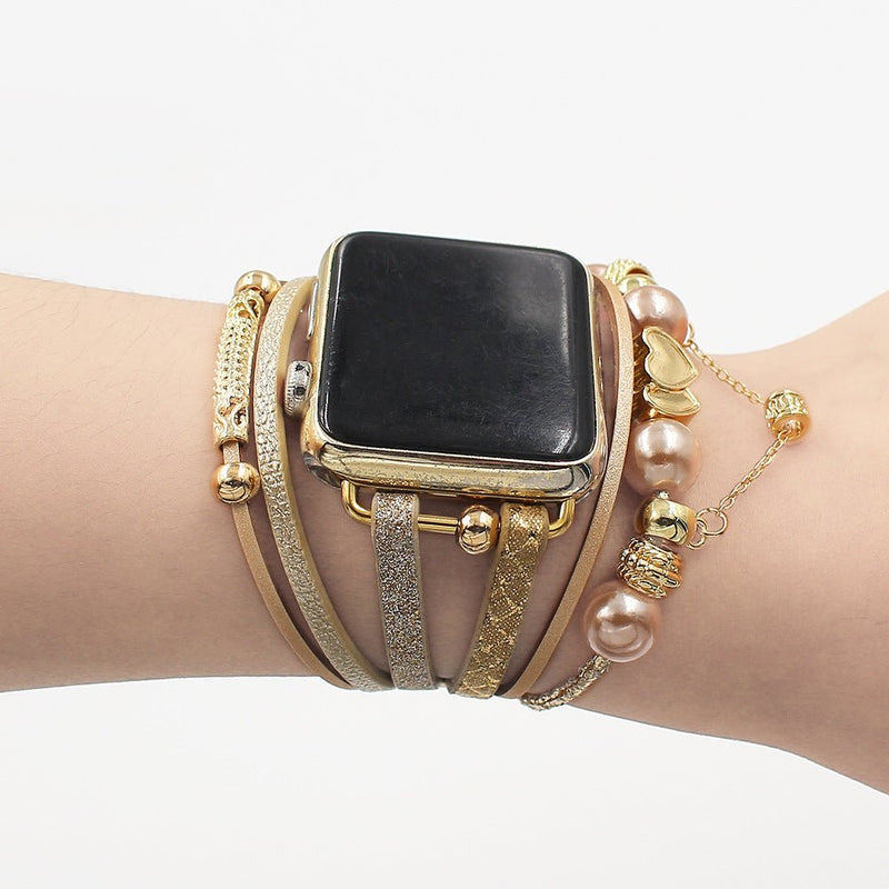 Bracelet multi-rangs or pour Apple Watch avec charms perles et cœur doré sur poignet femme.