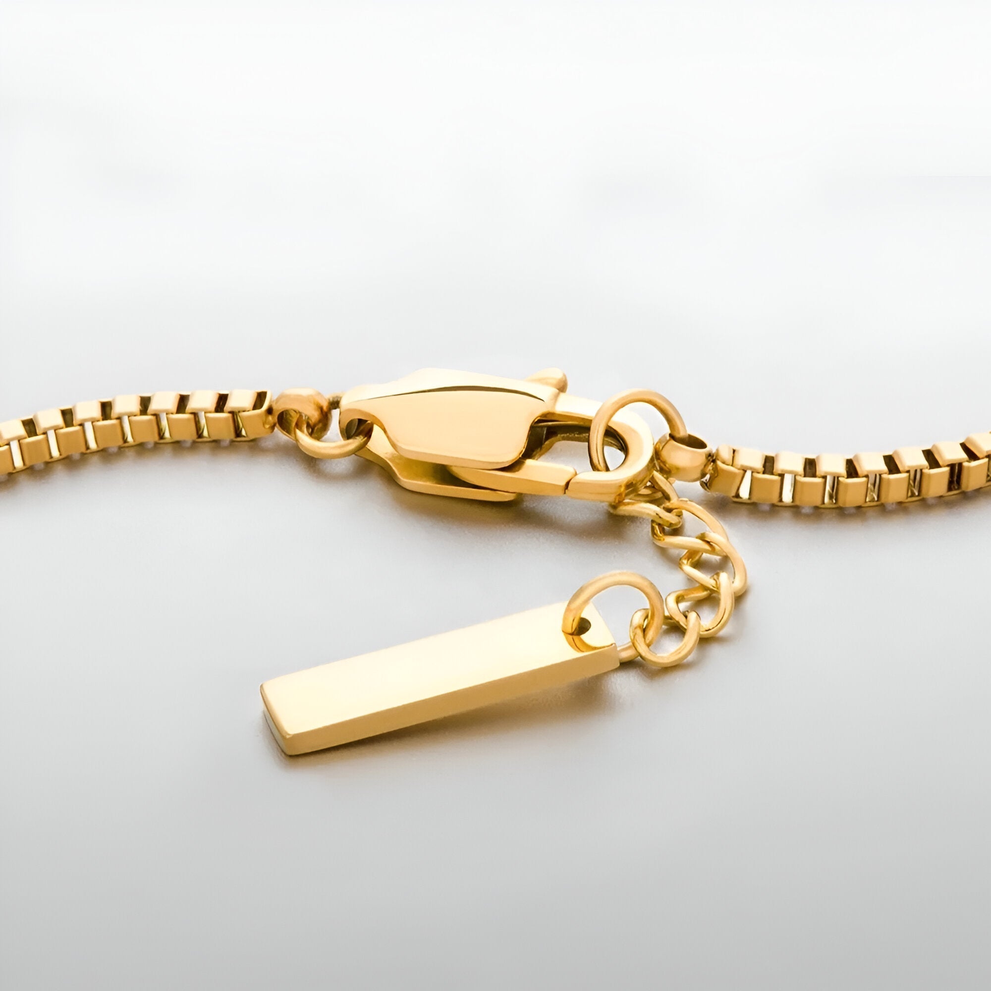 Bracelet homme en acier inoxydable doré, chaîne serpent avec fermoir mousqueton et pendentif rectangulaire lisse.