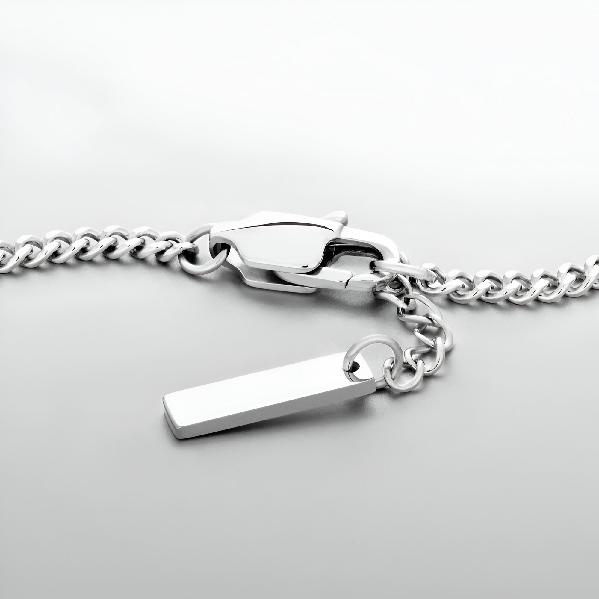 Bracelet homme en acier inoxydable argenté, maillons larges, fermoir coffre, pendentif rectangulaire fin.