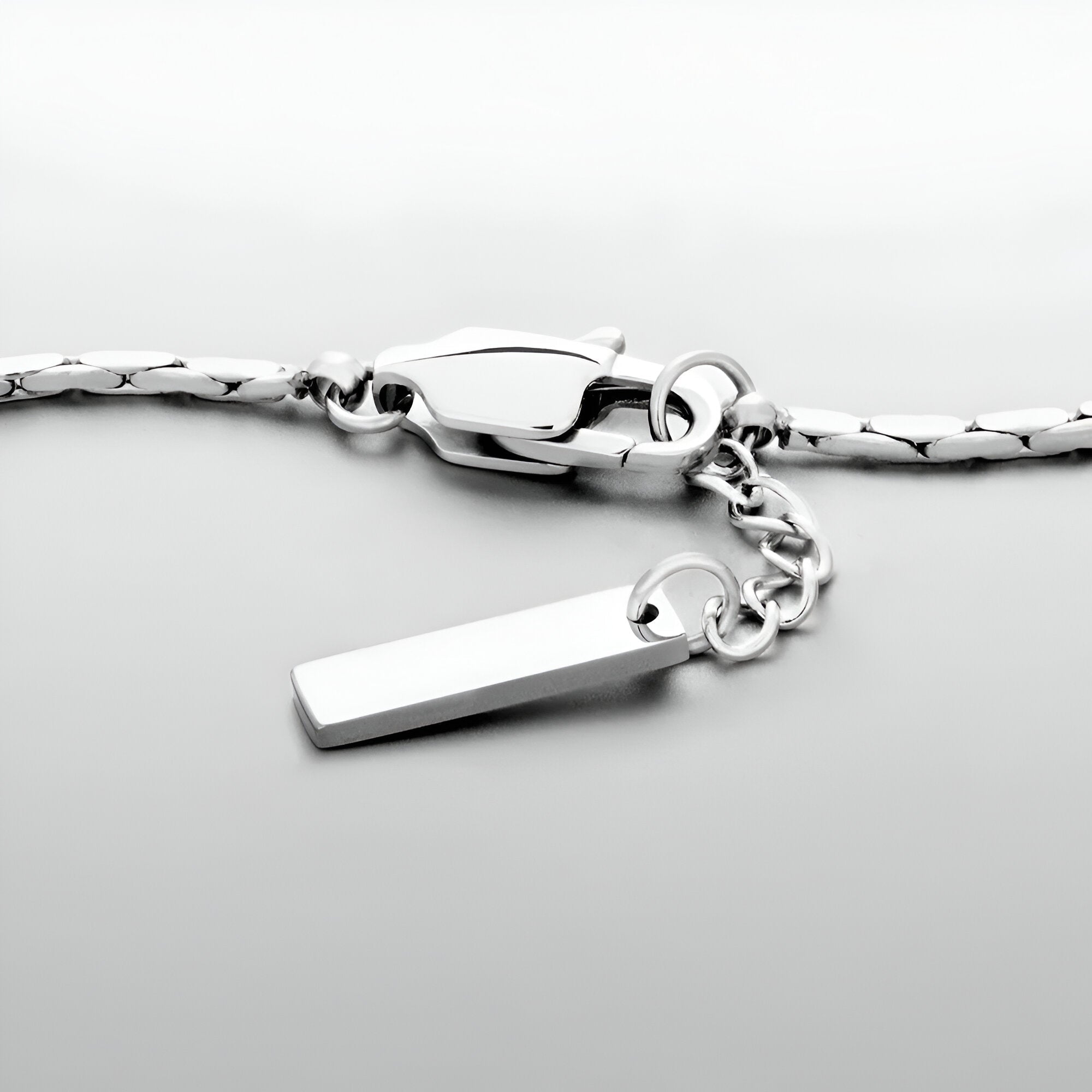 Bracelet en acier inoxydable argenté avec pendentif rectangulaire et fermoir mousqueton.