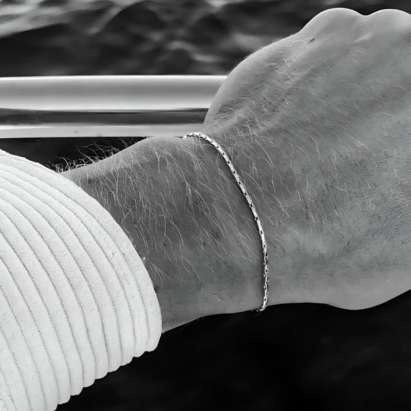 Bracelet fin doré en acier inoxydable lucide, modèle Julio, porté au poignet homme avec chemise blanche rayée.