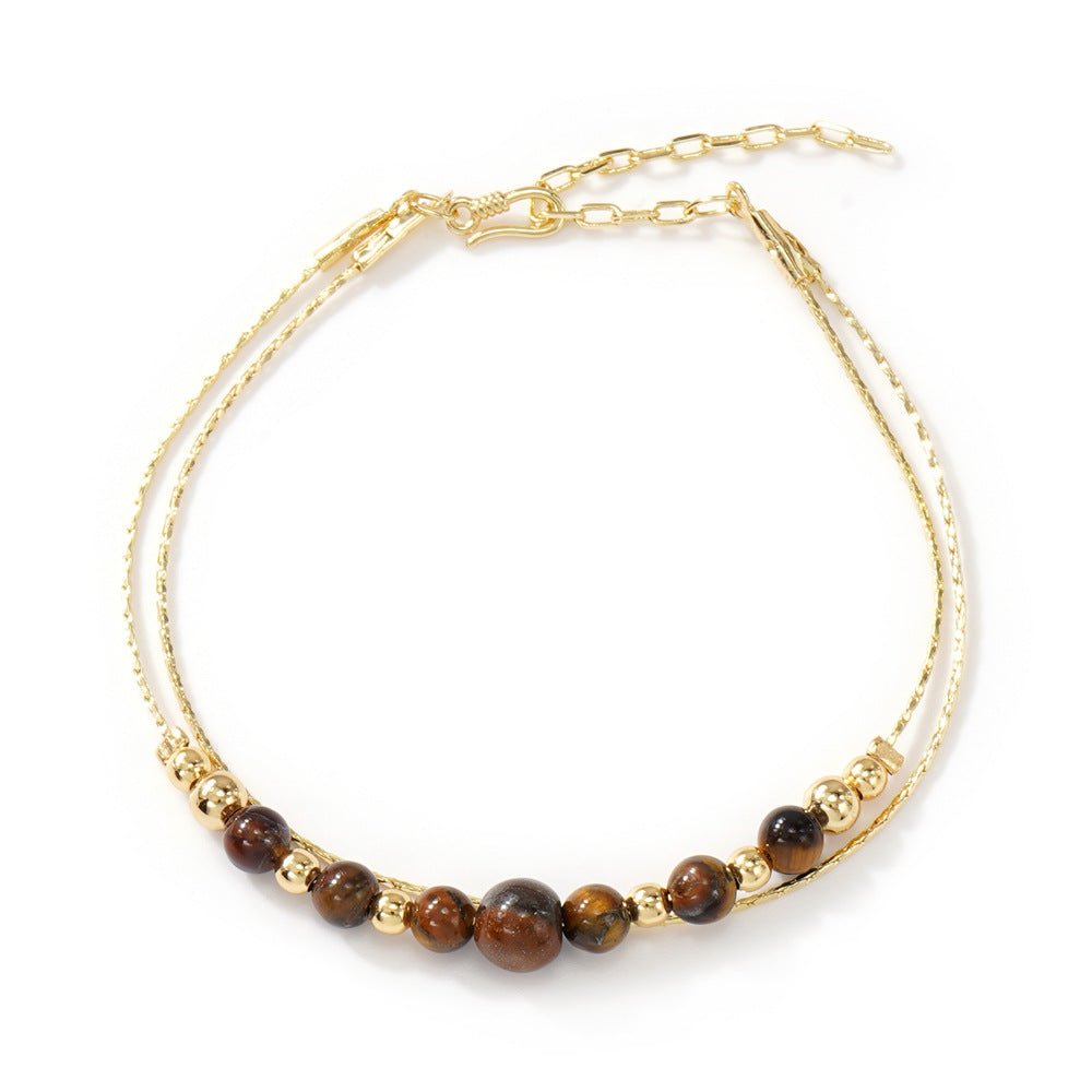 Bracelet double chaîne fine dorée avec perles rondes en œil de tigre brun, style minimaliste élégant.