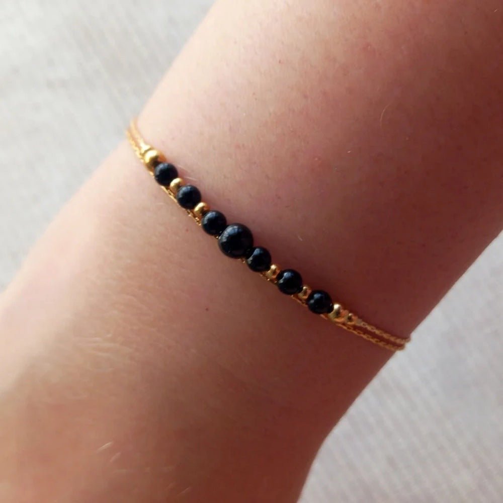 Bracelet double chaîne dorée avec perles rondes noires en onyx au centre, style minimaliste et élégant.