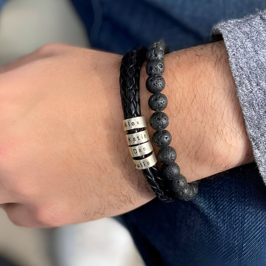Bracelet double cordon noir avec perles volcaniques et plaques métalliques arrondies gravées, porté au poignet.