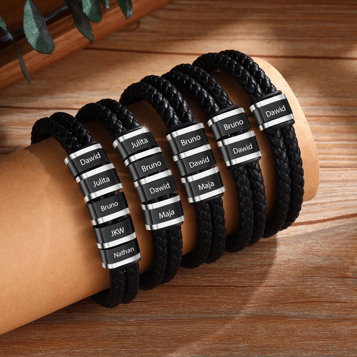 Bracelets double cordon cuir noir avec plaques métalliques gravées de prénoms variés.