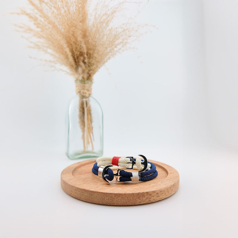 Bracelet double cordon bleu marine avec motif ancre large en métal argenté, style marin, posé sur socle rond en liège.