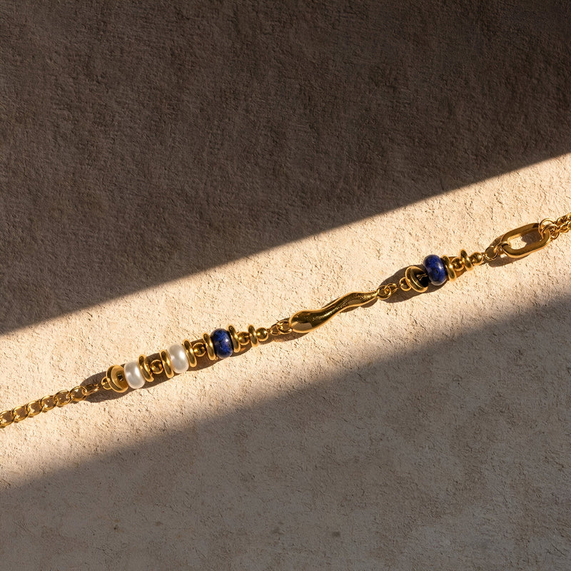 Bracelet double en acier inoxydable doré avec perles en lapis lazuli bleu profond et détails tordus élégants.