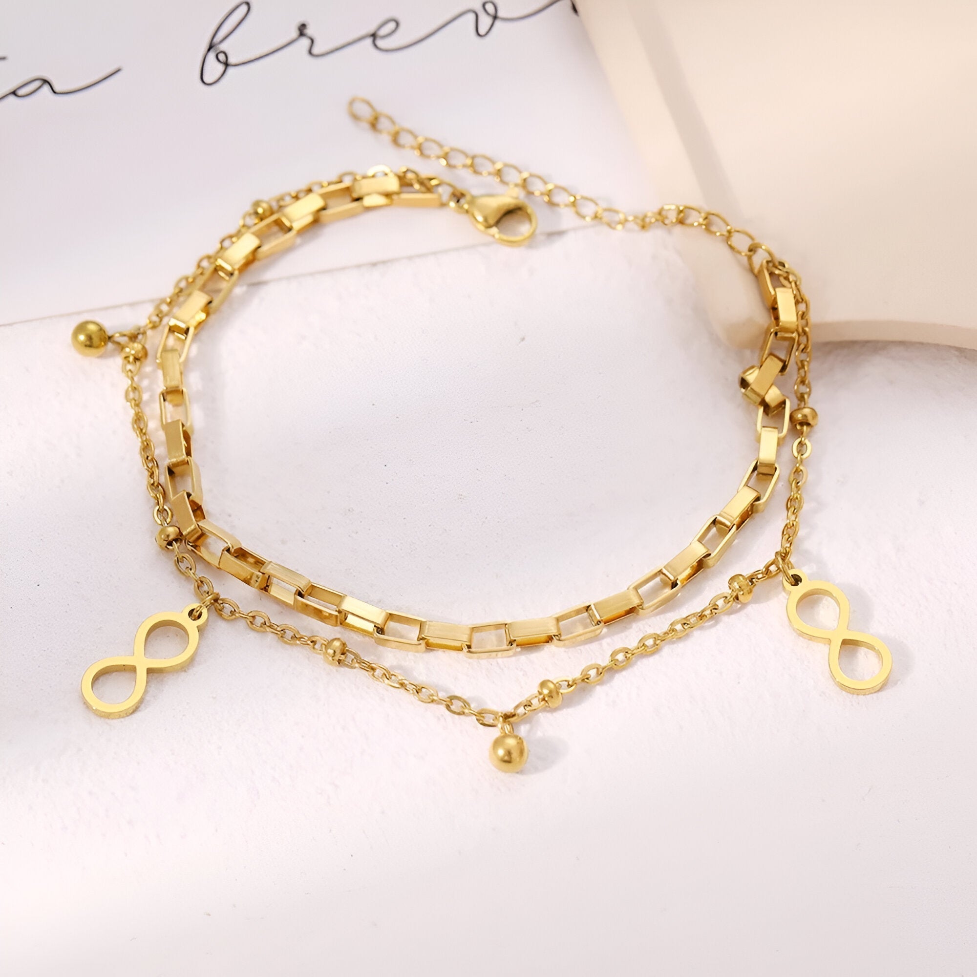 Bracelet double chaîne en acier inoxydable doré avec charms infini et pendentif boule délicat.