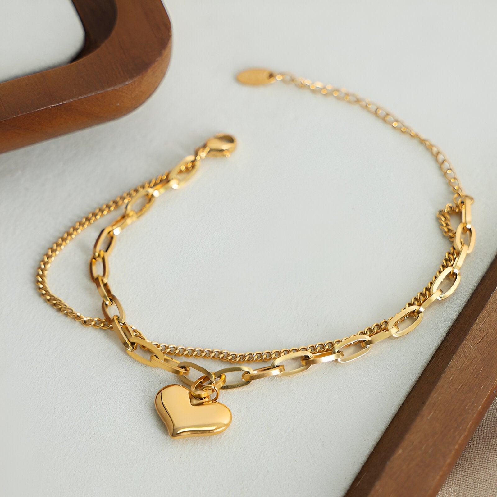 Bracelet double en titane plaqué or avec pendentif cœur lisse, chaînes fines et maille alternée.