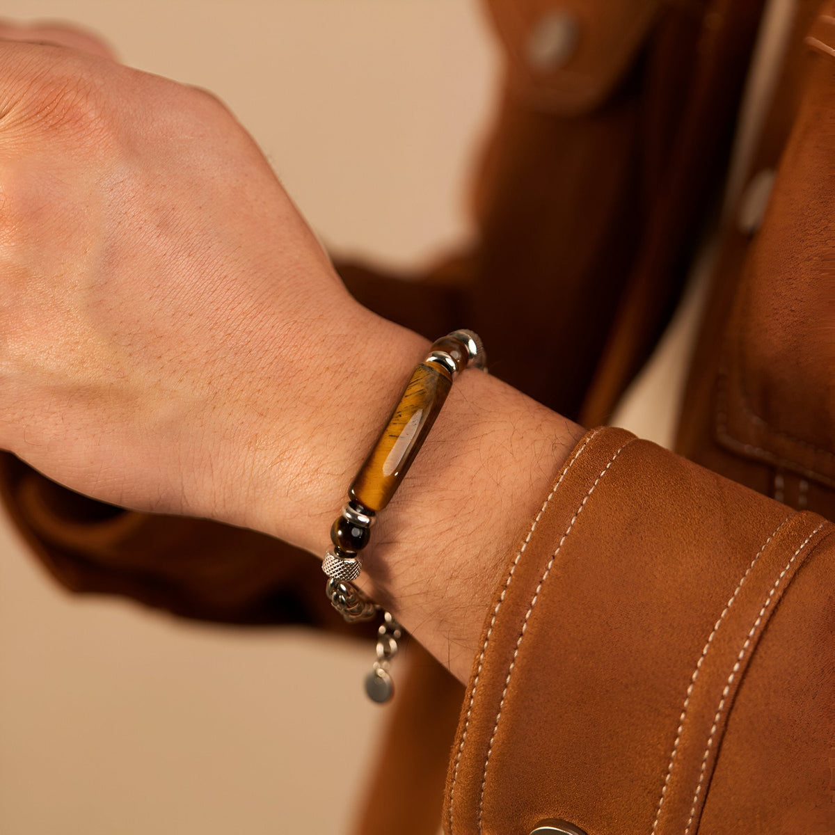Bracelet homme en acier inoxydable argenté avec perles d’œil de tigre marron et noirs, détail pendentif rond.