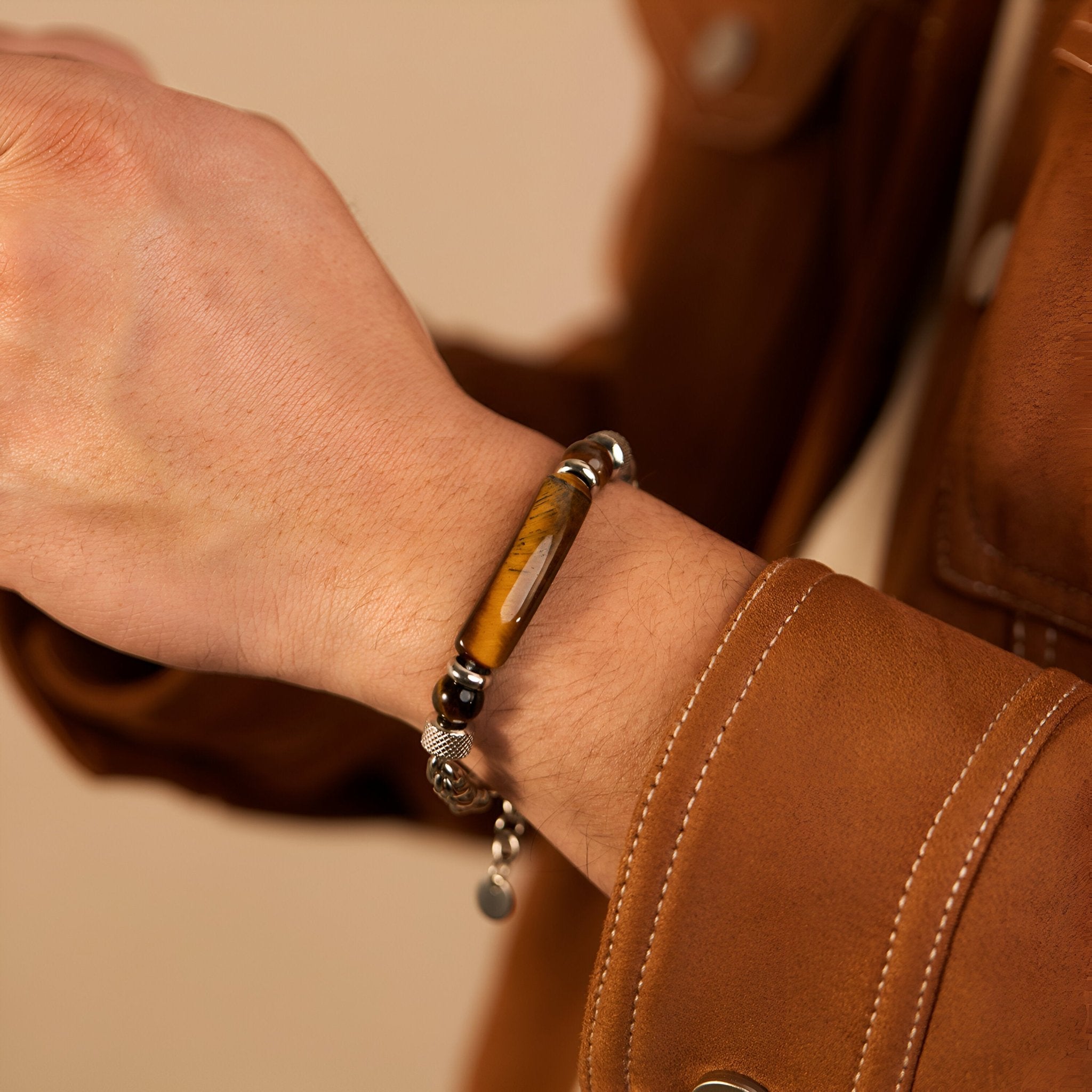 Bracelet homme en acier inoxydable argenté avec perles d’œil de tigre marron et noirs, détail pendentif rond.