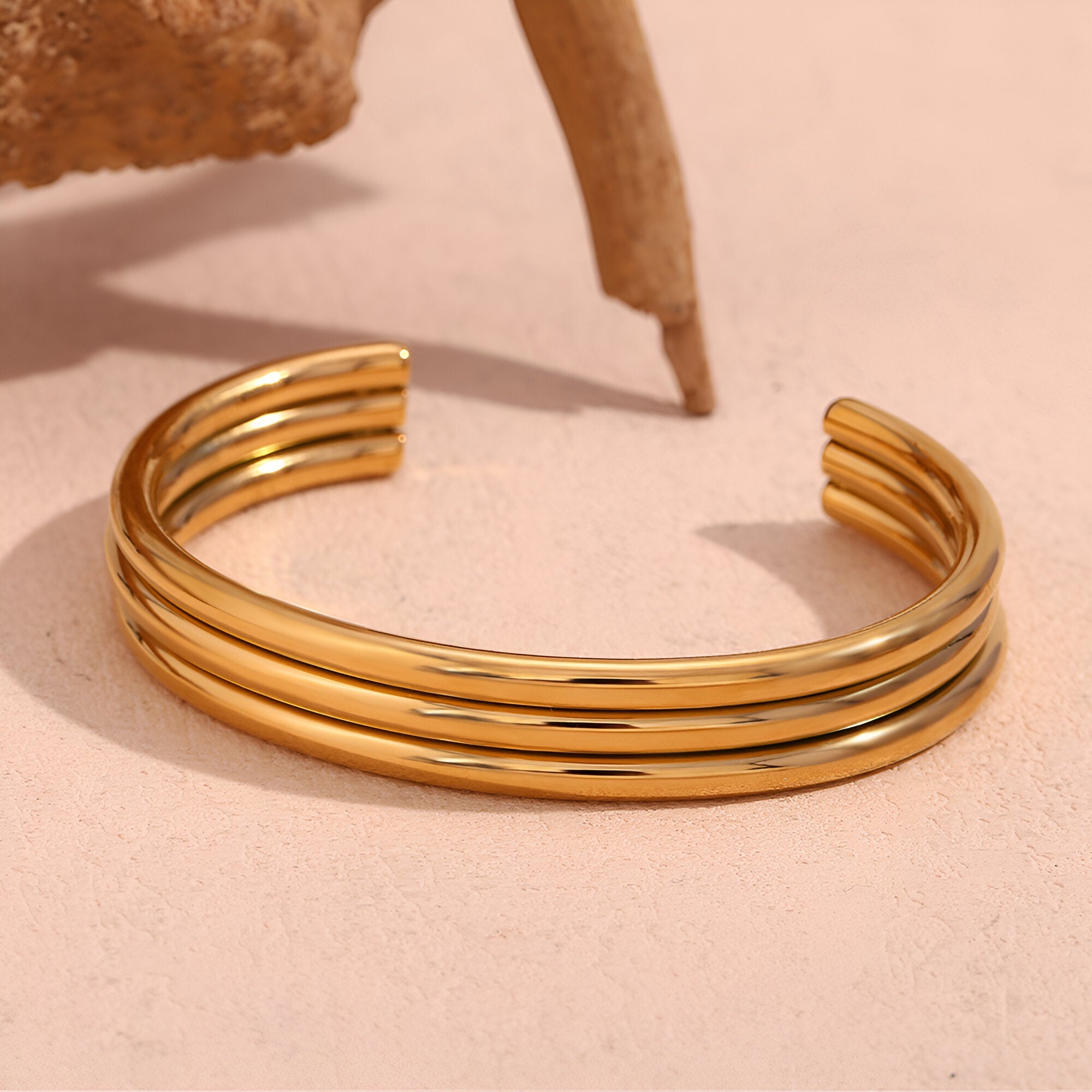 Bracelet rigide en acier inoxydable plaqué or 18 carats avec trois anneaux lisses et incurvés, modèle Amaya.