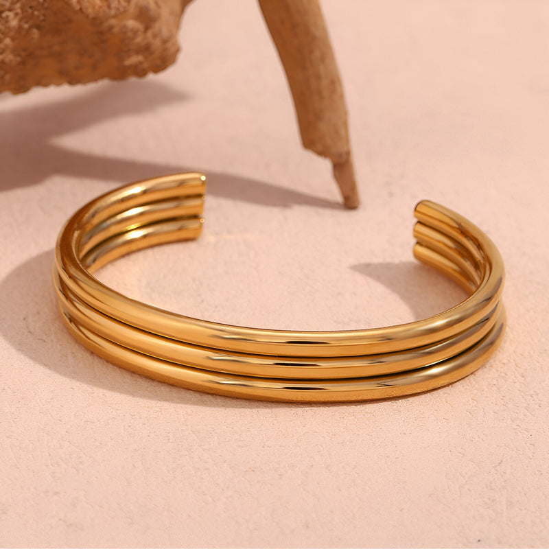 Bracelet rigide en acier inoxydable plaqué or 18 carats avec trois anneaux lisses et incurvés, modèle Amaya.