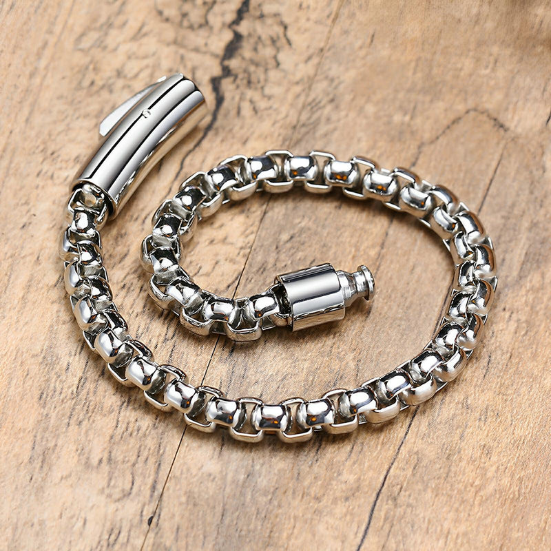 Bracelet en maille rolo épaisse en acier inoxydable argenté avec fermoir tubulaire sur bois clair.