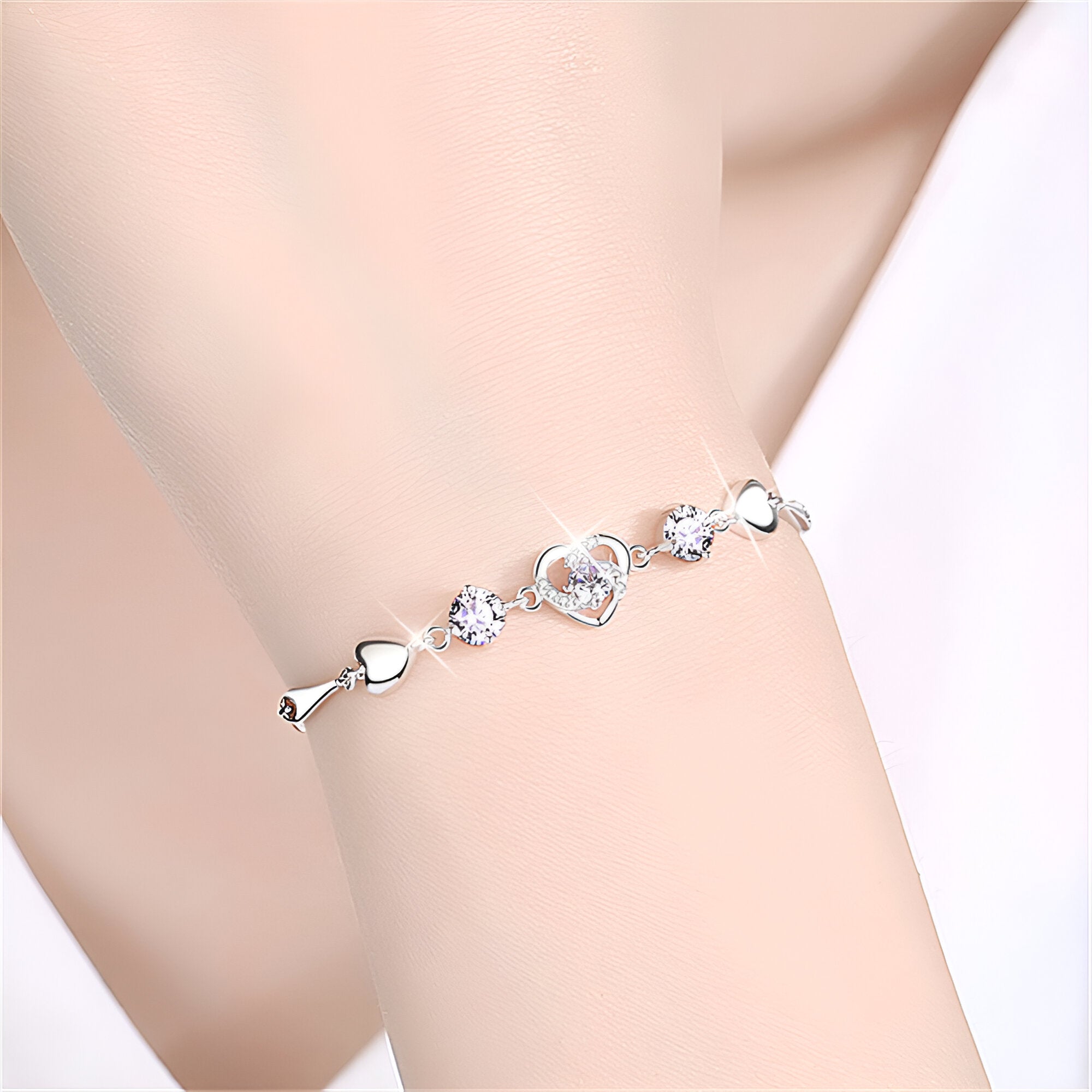 Bracelet fin en argent avec charms cœur et cristaux brillants sur poignet féminin.