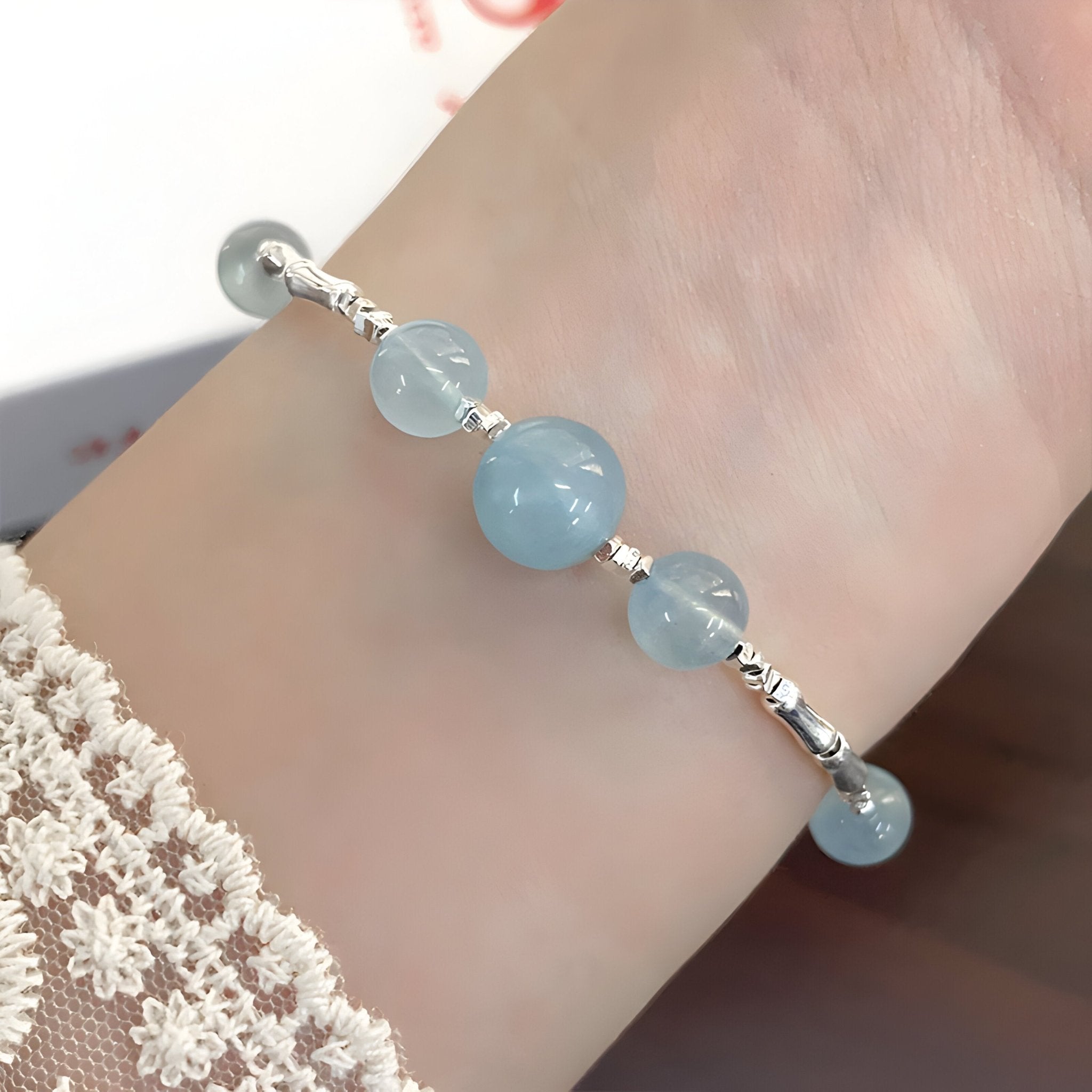 Bracelet fin en argent sterling avec trois pierres rondes d'aigue-marine bleu clair sur poignet féminin.