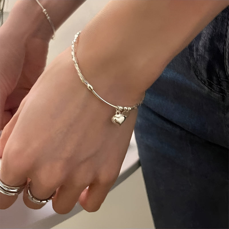 Bracelet fin en argent sterling avec pendentif cœur brillant porté au poignet féminin.
