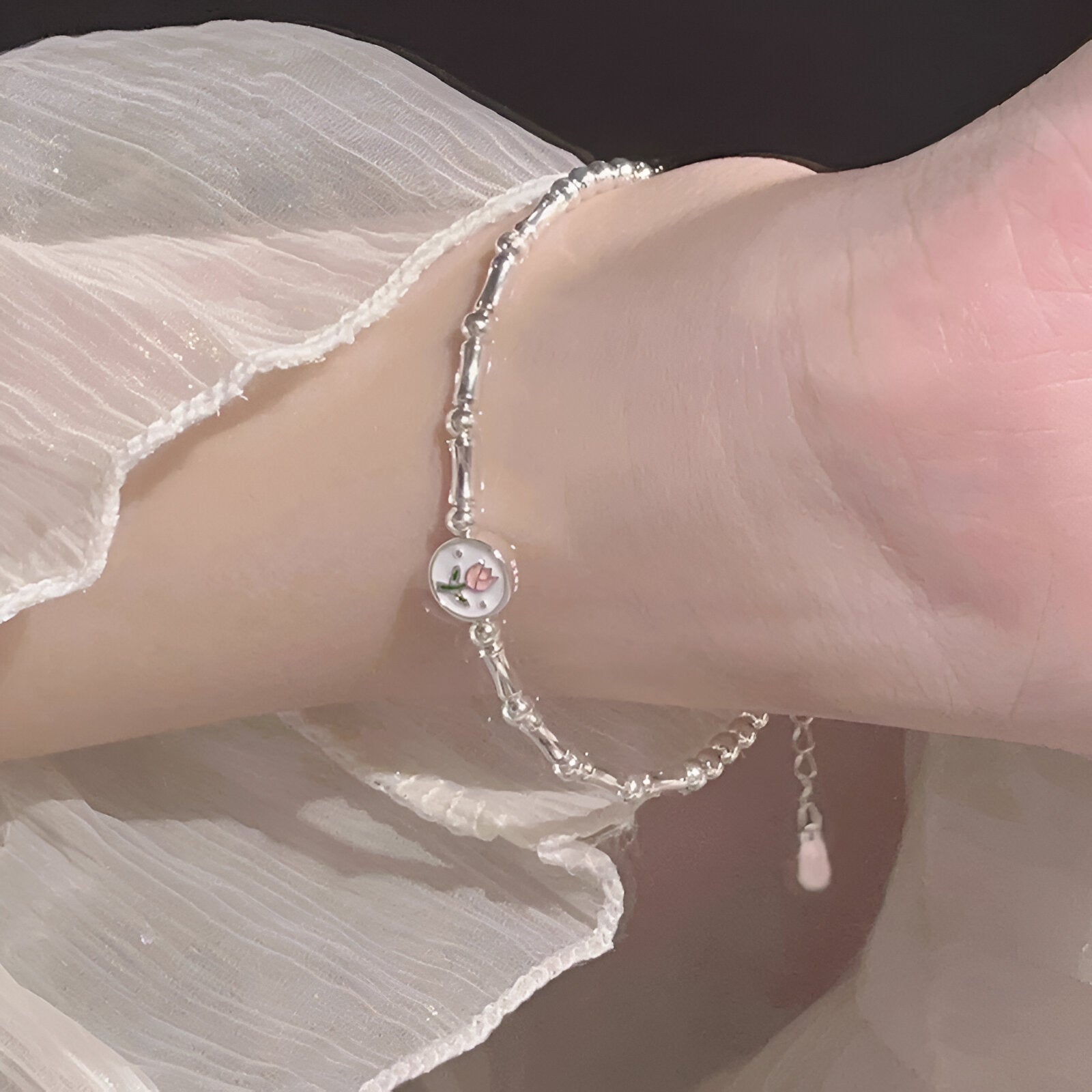 Bracelet fin en argent sterling avec charm tulipe délicate, porté au poignet féminin.