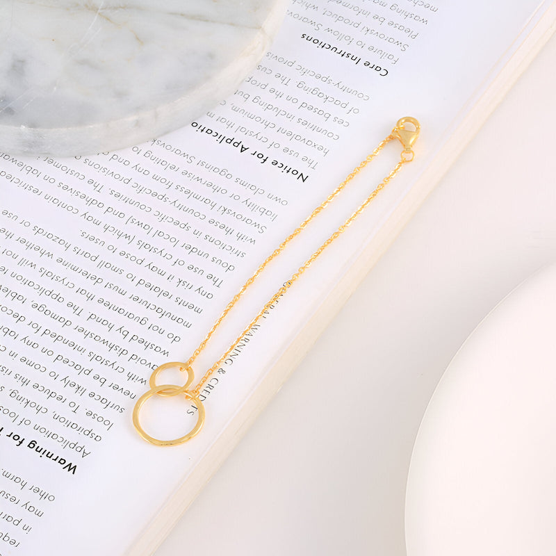 Bracelet en or avec duo de cercles entrelacés suspendus à une chaîne fine délicate.