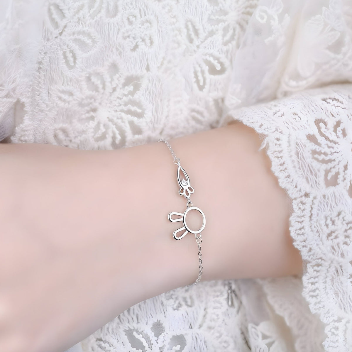 Bracelet en argent sterling avec pendentif lapin et carotte délicat porté sur poignet féminin en dentelle blanche.