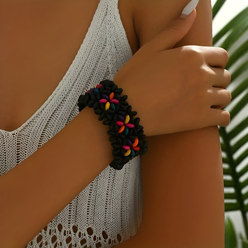Bracelet en bois noir avec motif floral coloré porté sur poignet féminin en maillot ivoire ajouré.