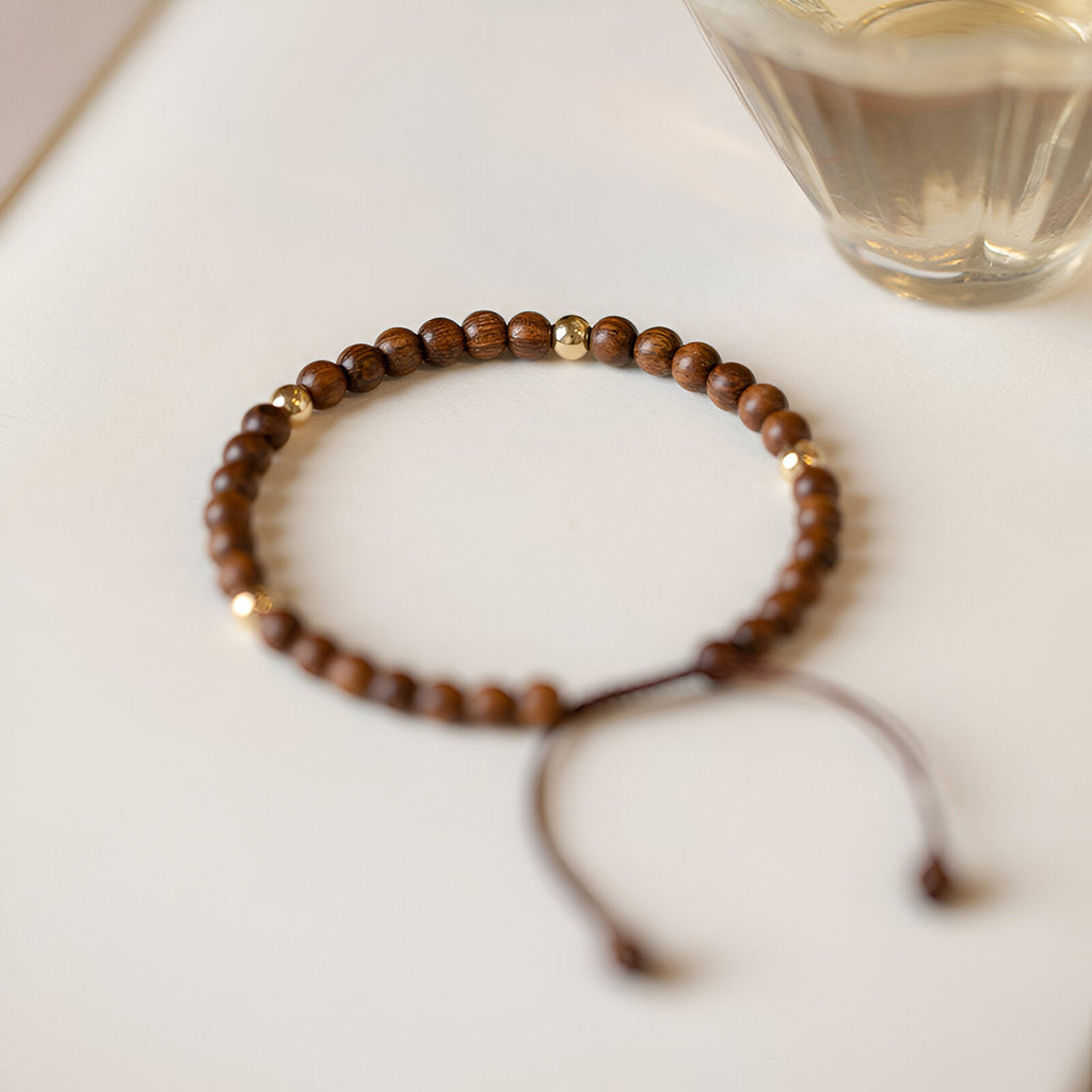 Bracelet femme en perles rondes de bois de santal marron avec deux perles dorées et cordon ajustable.