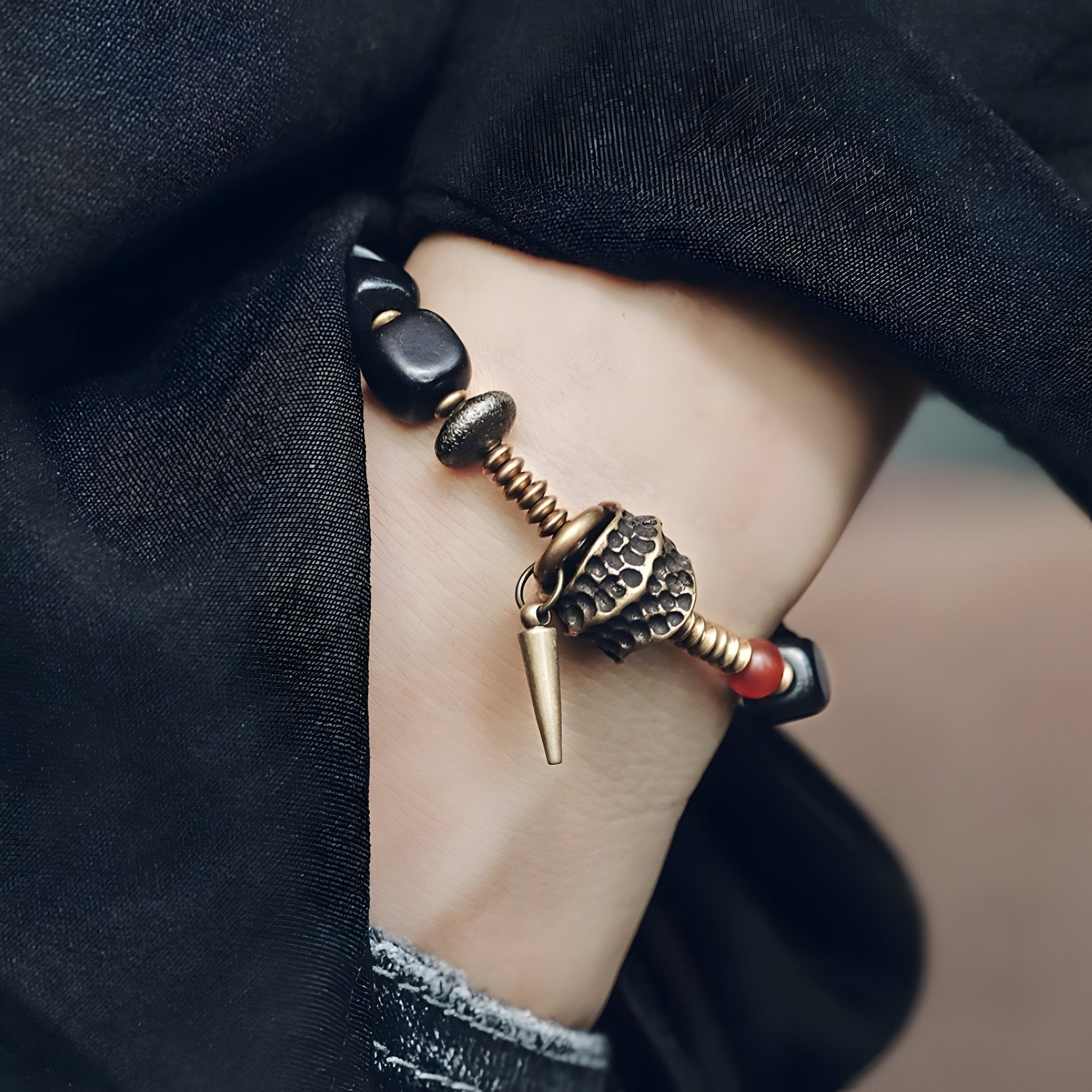 Bracelet en bois d'ébène noir avec pendentif antique en métal doré et perles décoratives sur poignet féminin.