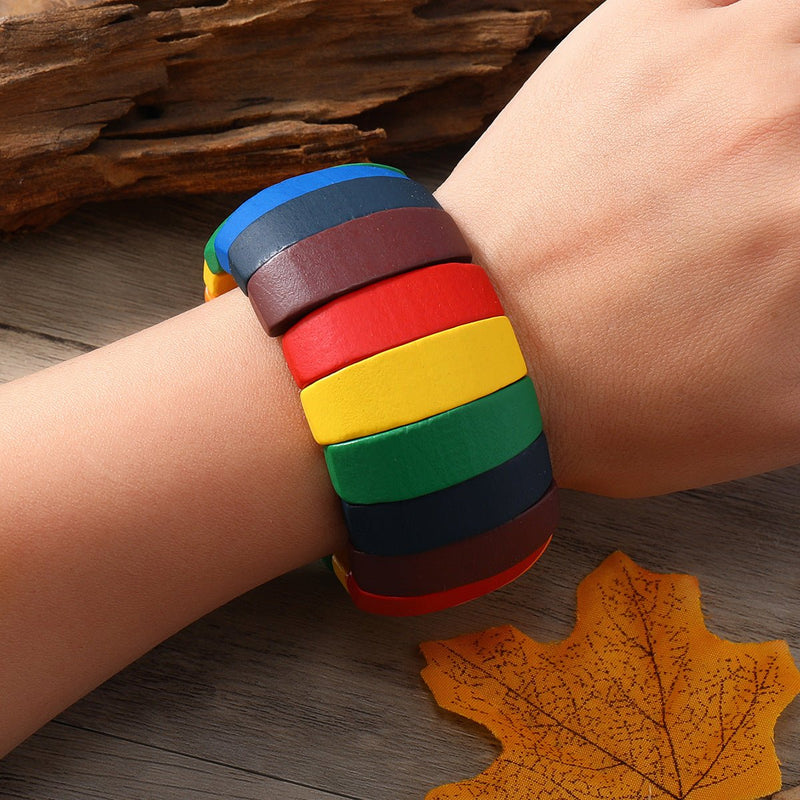 Bracelet en bois naturel multicolore avec larges segments bleu, marron, rouge, jaune et vert sur poignet féminin.