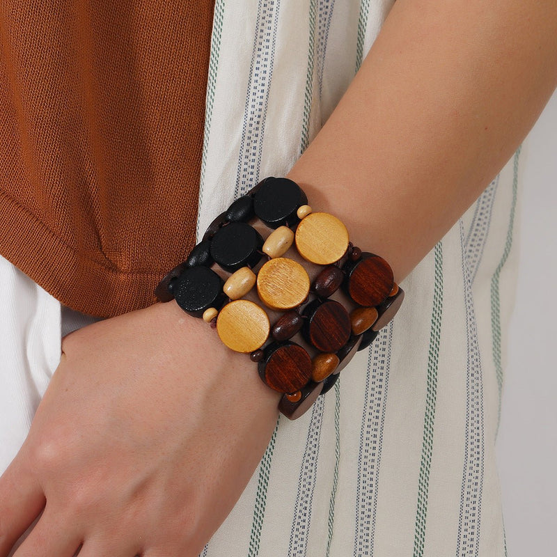 Bracelet large en bois naturel avec gros cercles noirs, jaunes et marron porté au poignet féminin.