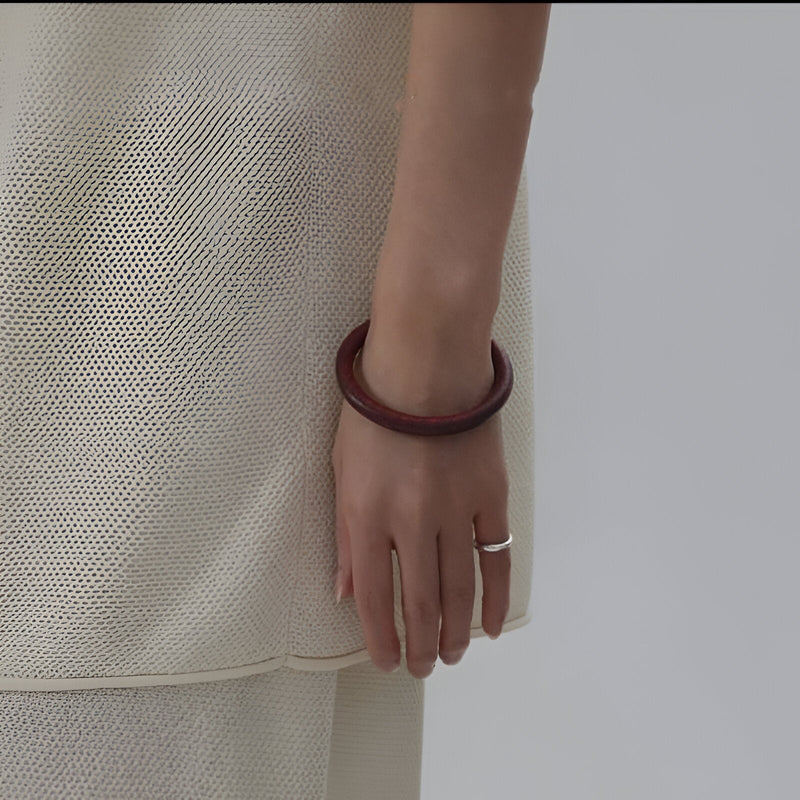 Jonc bracelet en bois marron foncé lisse porté au poignet femme, style naturel et élégant.