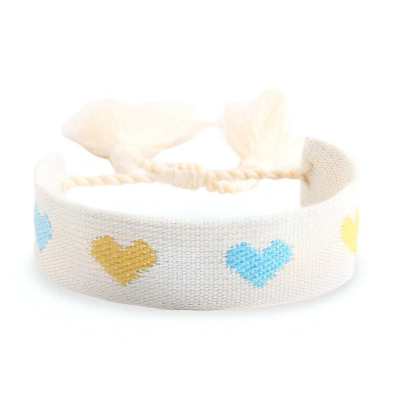 Bracelet en corde tressée blanche avec motifs de cœurs jaunes et bleus et pompon en macramé.