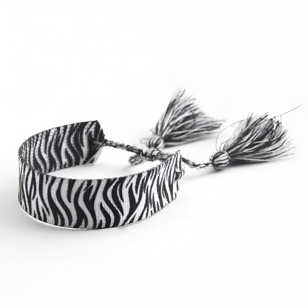 Bracelet en corde tressée blanc à motif zèbre noir avec pompons assortis.