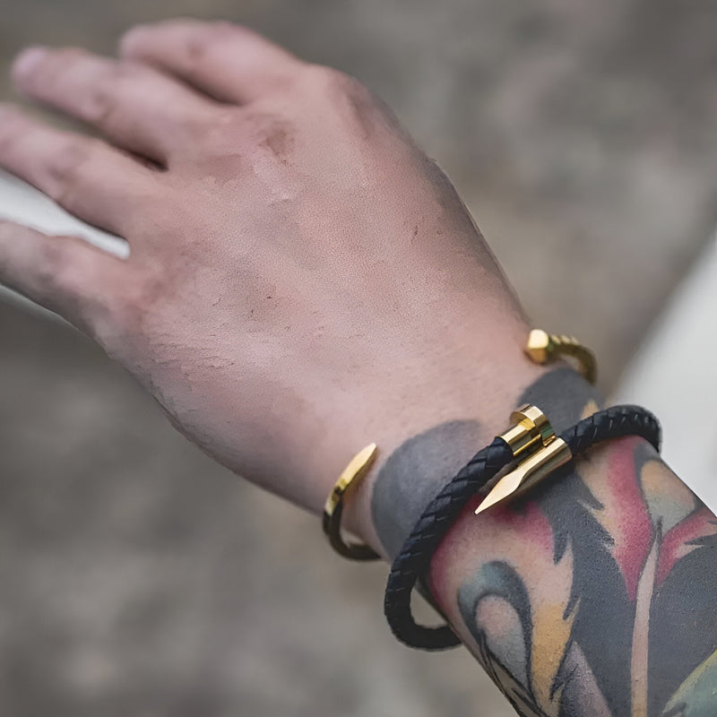 Bracelet en cuir noir avec extrémités en cône dorées, style Paul, porté au poignet homme tatoué.