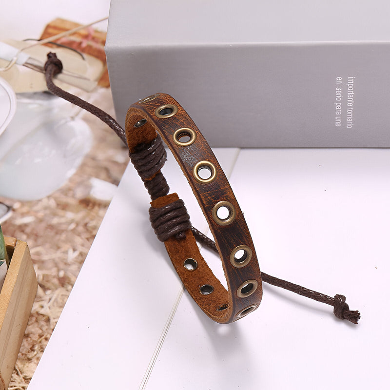 Bracelet en cuir marron avec anneaux métalliques incrustés et fermeture ajustable par cordon.